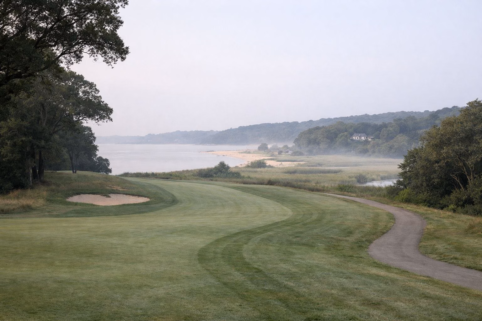 A golf fairway curving between mature oak woods on gently rolling hills, light morning mist, no golfers close up