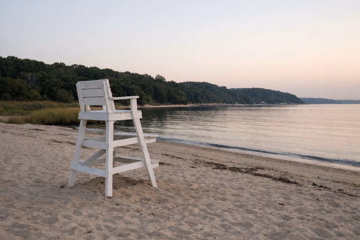 An empty white wooden lifeguard chair on a sand beach at evening, calm water behind, nobody around