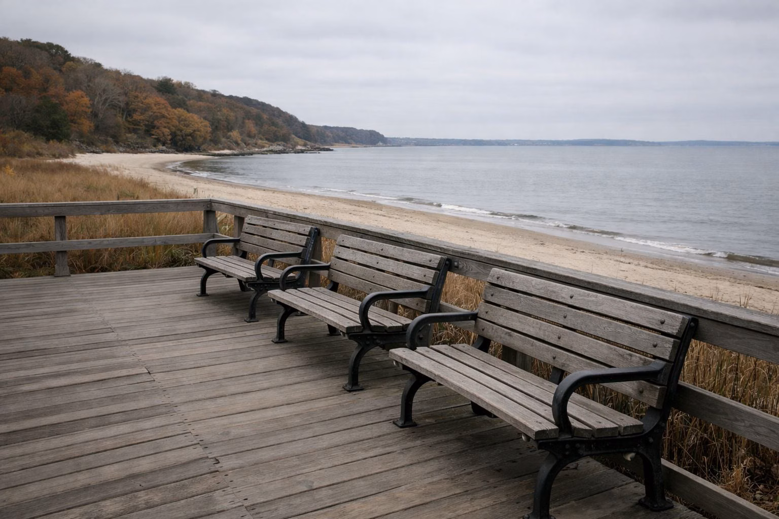 Empty wooden benches along a boardwalk overlooking a quiet beach on an overcast day